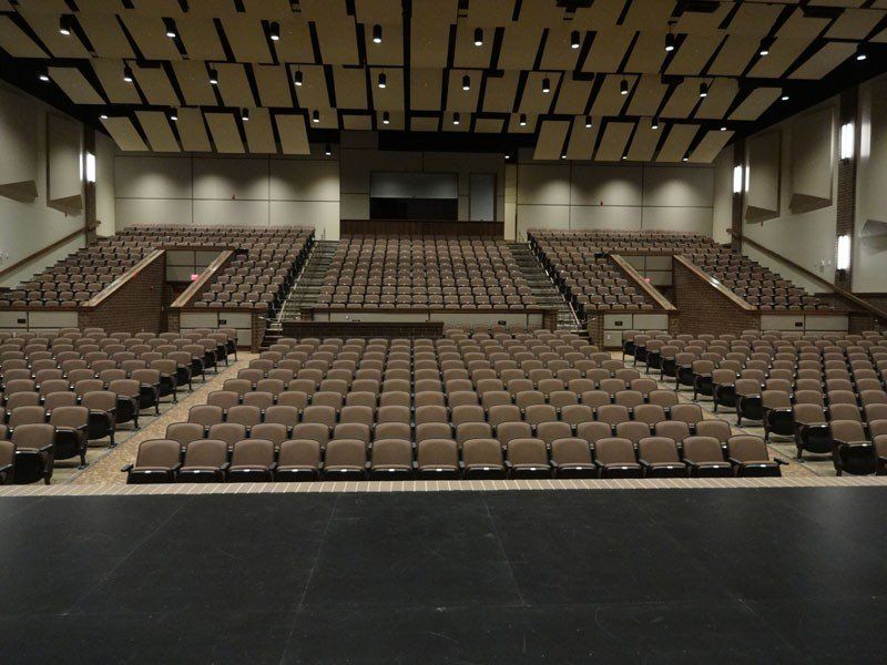 Empty auditorium with rows of tan seats, stage in front, and acoustic wall panels overhead