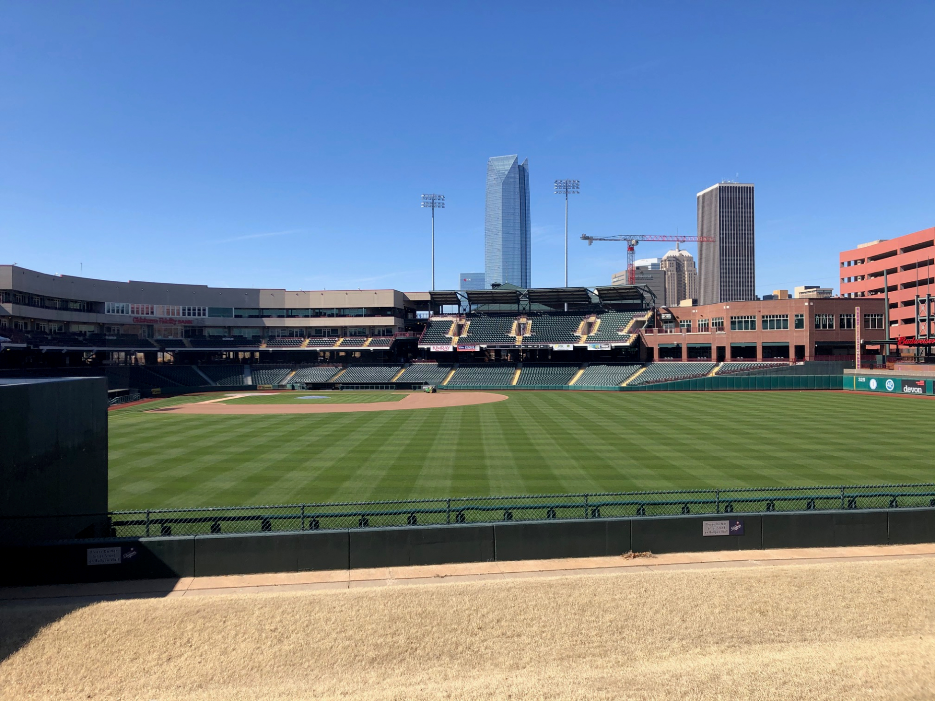 Empty baseball stadium field with green turf, stands, and a city skyline in the background