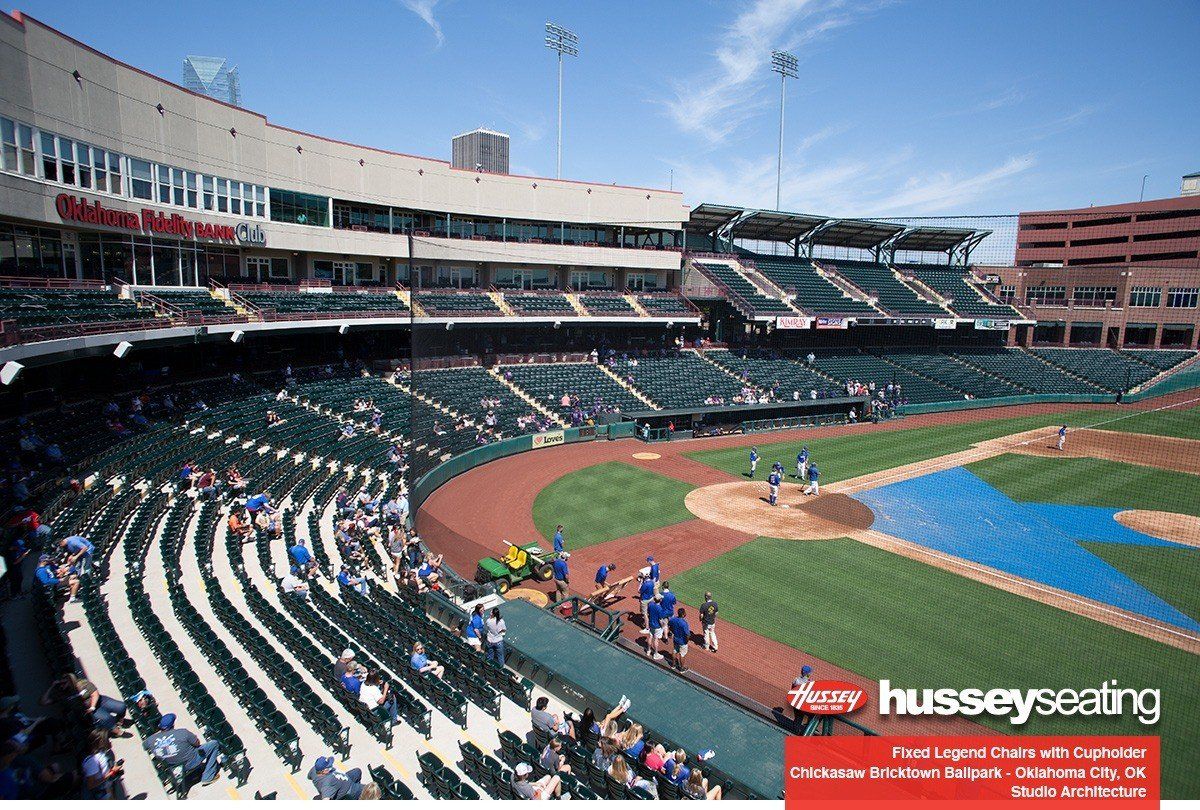 Baseball stadium with players on the field and fans seated in the stands, viewed from behind home plate