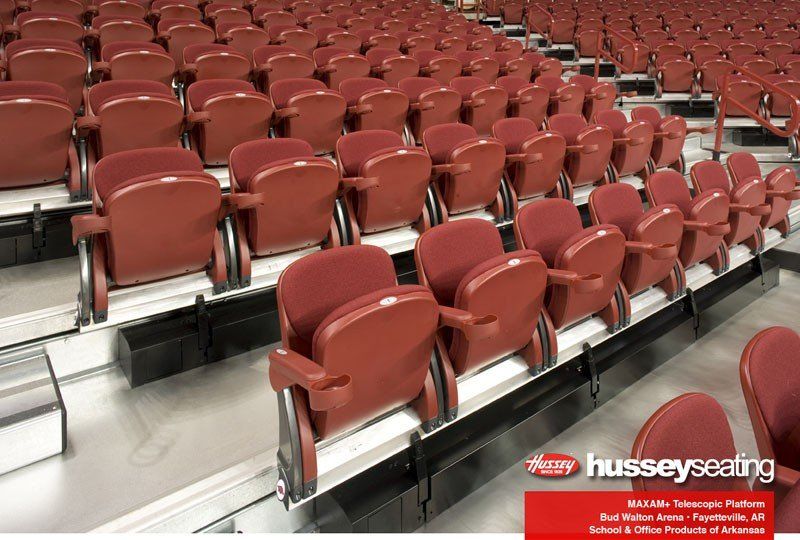Rows of empty red stadium seats with silver armrests in an indoor arena