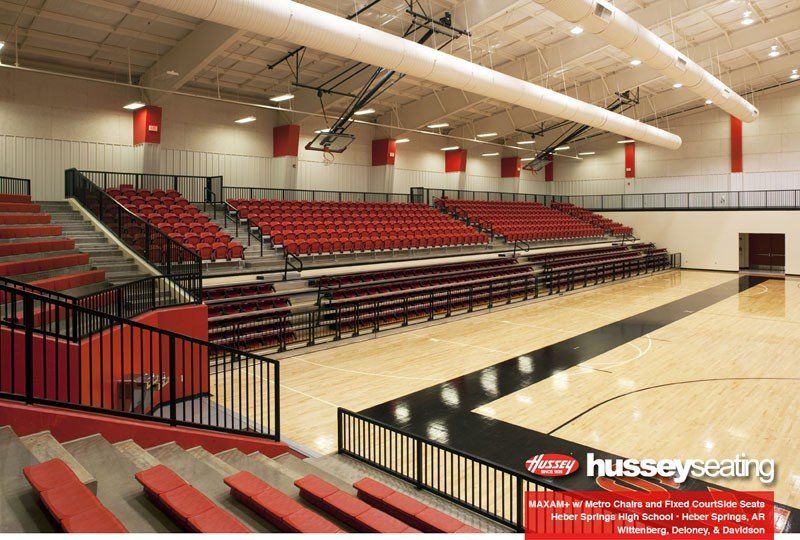 Empty school gymnasium with red bleachers and polished wooden floor