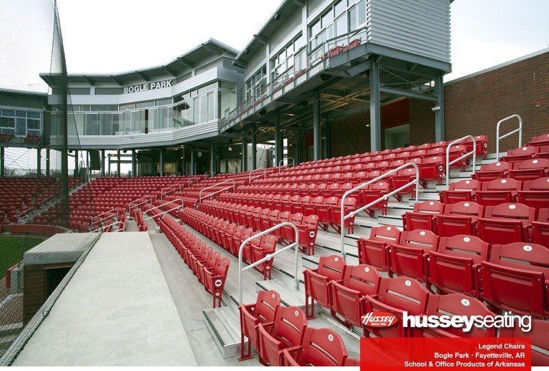 Red stadium seats beside a concrete walkway under a modern grandstand structure
