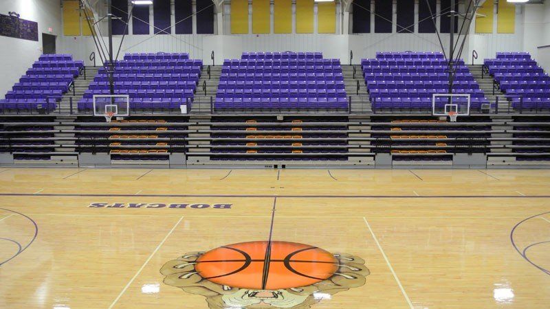 Empty basketball court with purple bleachers and two hoops in an indoor gym