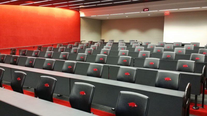 Empty lecture hall with rows of gray seats and a red accent wall.