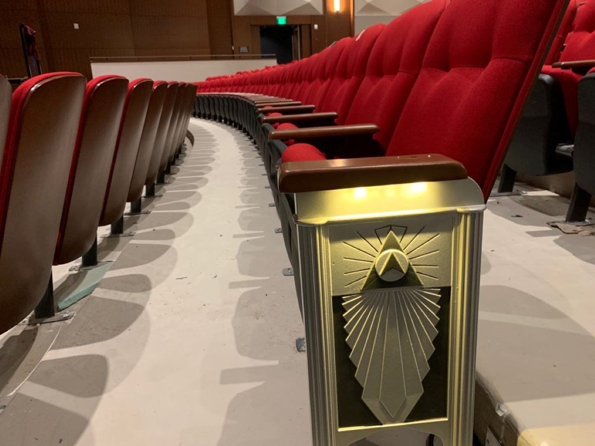 Row of red theater seats beside a decorative aisle light in a dim cinema auditorium