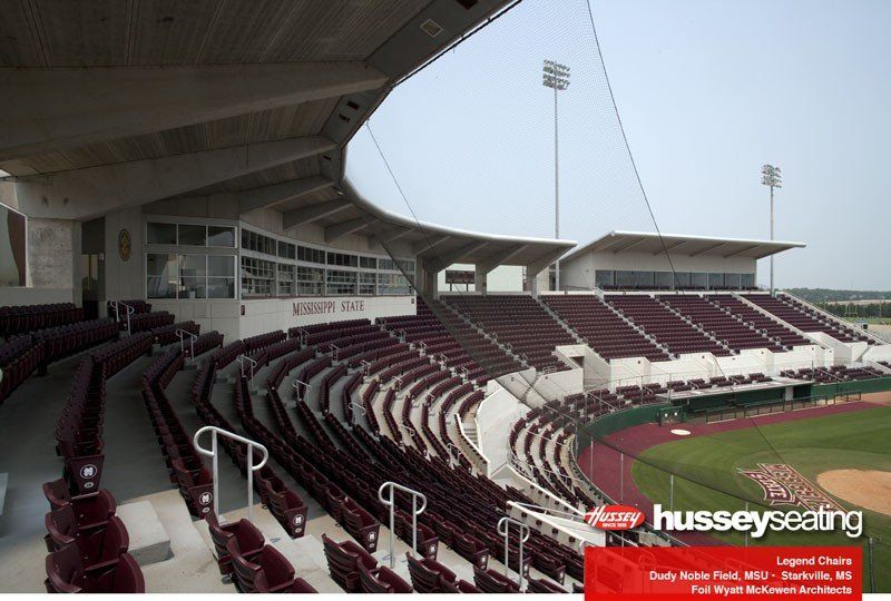 Empty stadium seating with maroon seats under a covered grandstand, viewed from the stands across the field