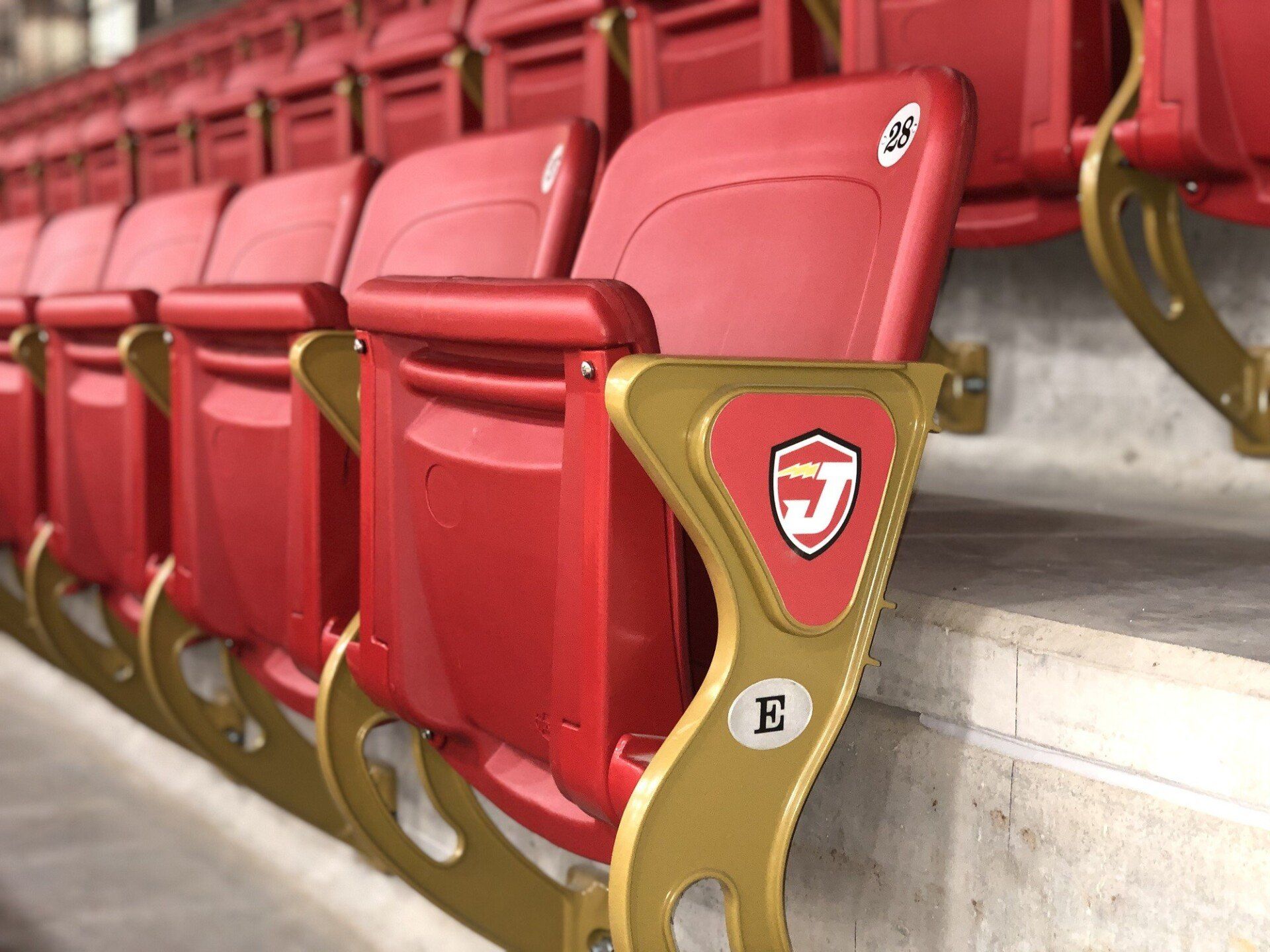 Red stadium seats with gold metal armrests in an empty arena row
