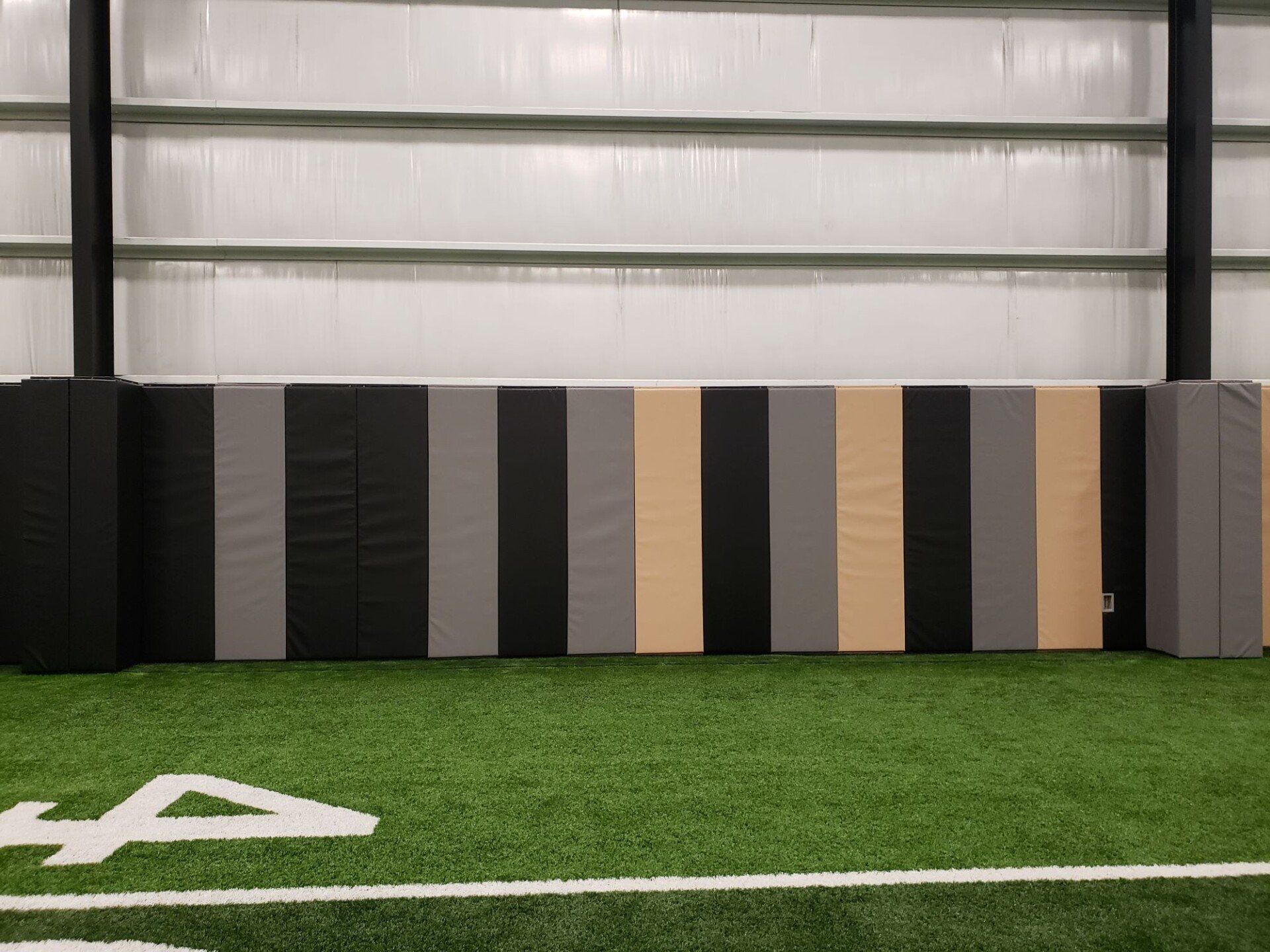 Indoor turf field wall with alternating black, gray, tan, and beige padded panels