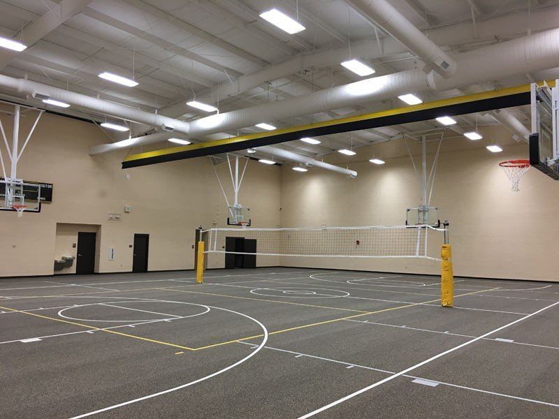 Indoor gymnasium with a volleyball net over a basketball court and overhead lights