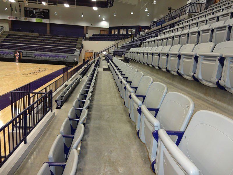 Empty indoor basketball arena with gray bleachers and court seating rows