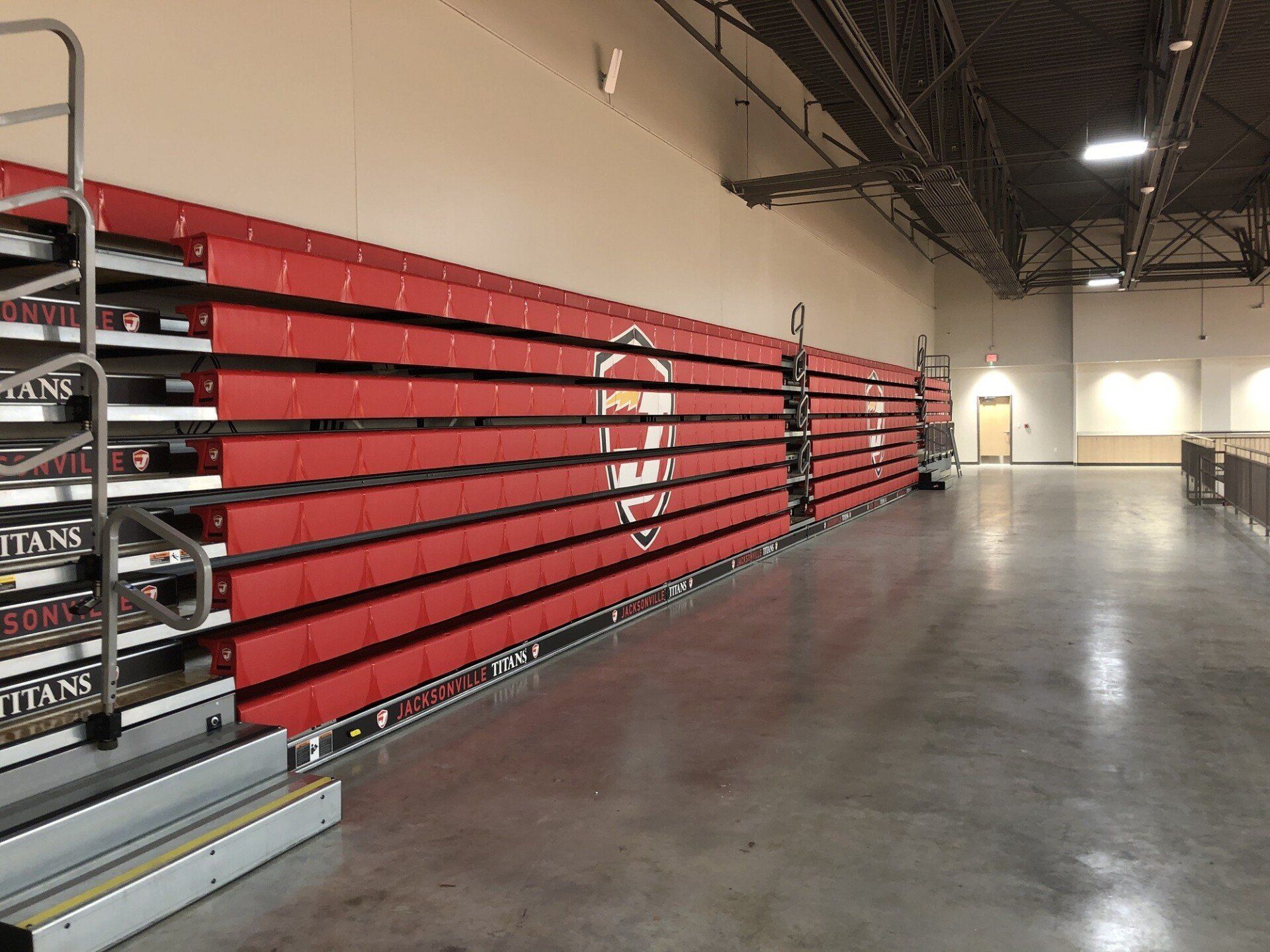 Empty indoor arena with red bleachers along one wall and a polished concrete floor