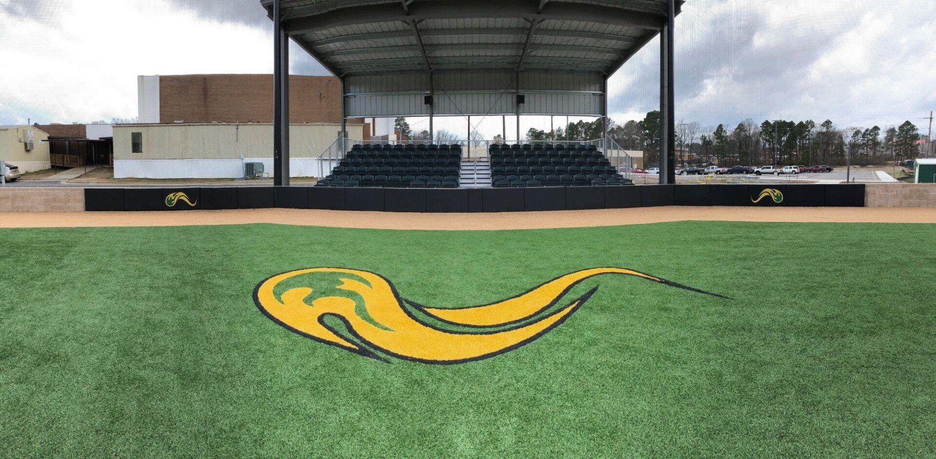 Empty covered stadium stands behind a green field with a yellow logo at center