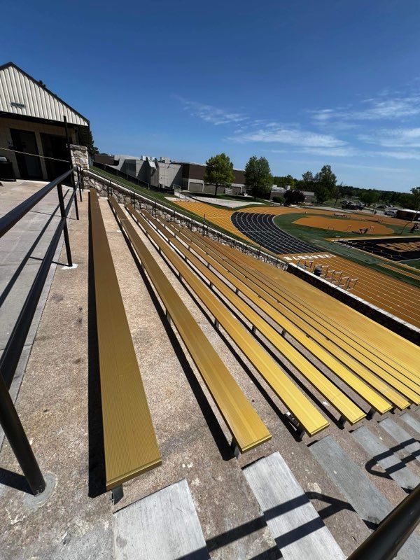 Rows of yellow and black stadium bleachers under a blue sky, viewed from the stands.