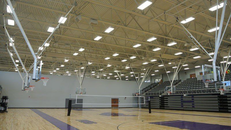 Empty indoor gymnasium with basketball hoops, bleachers, and polished wood floor