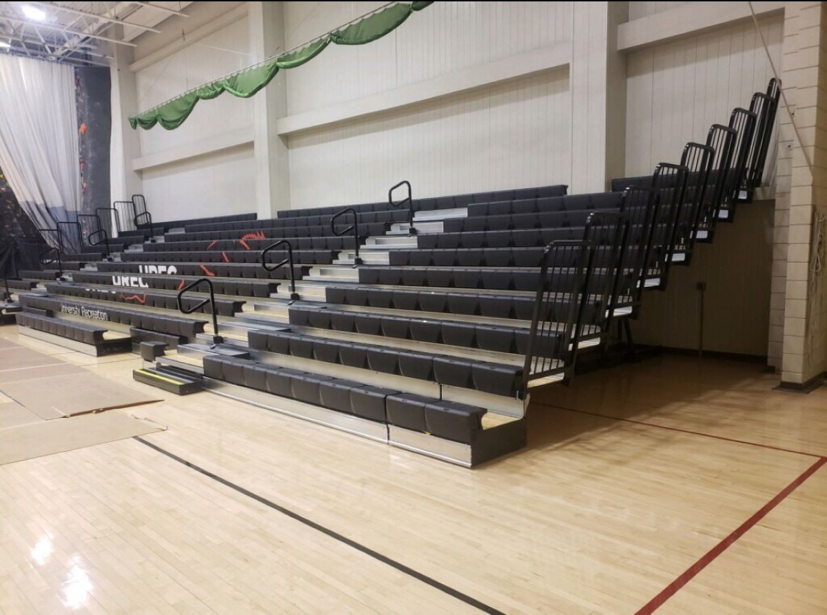 Indoor gymnasium with folded black bleachers beside a polished wood court