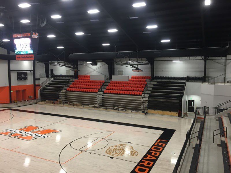 Indoor basketball court with red-and-black bleachers and bright overhead lights