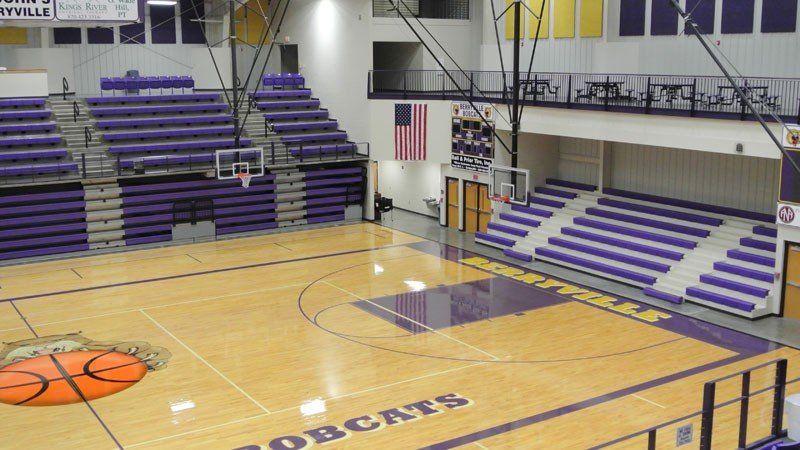 Empty indoor basketball gym with purple bleachers and a polished wood court