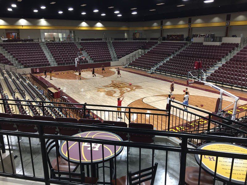 Empty indoor basketball arena with maroon seats and a light wood court under bright overhead lights
