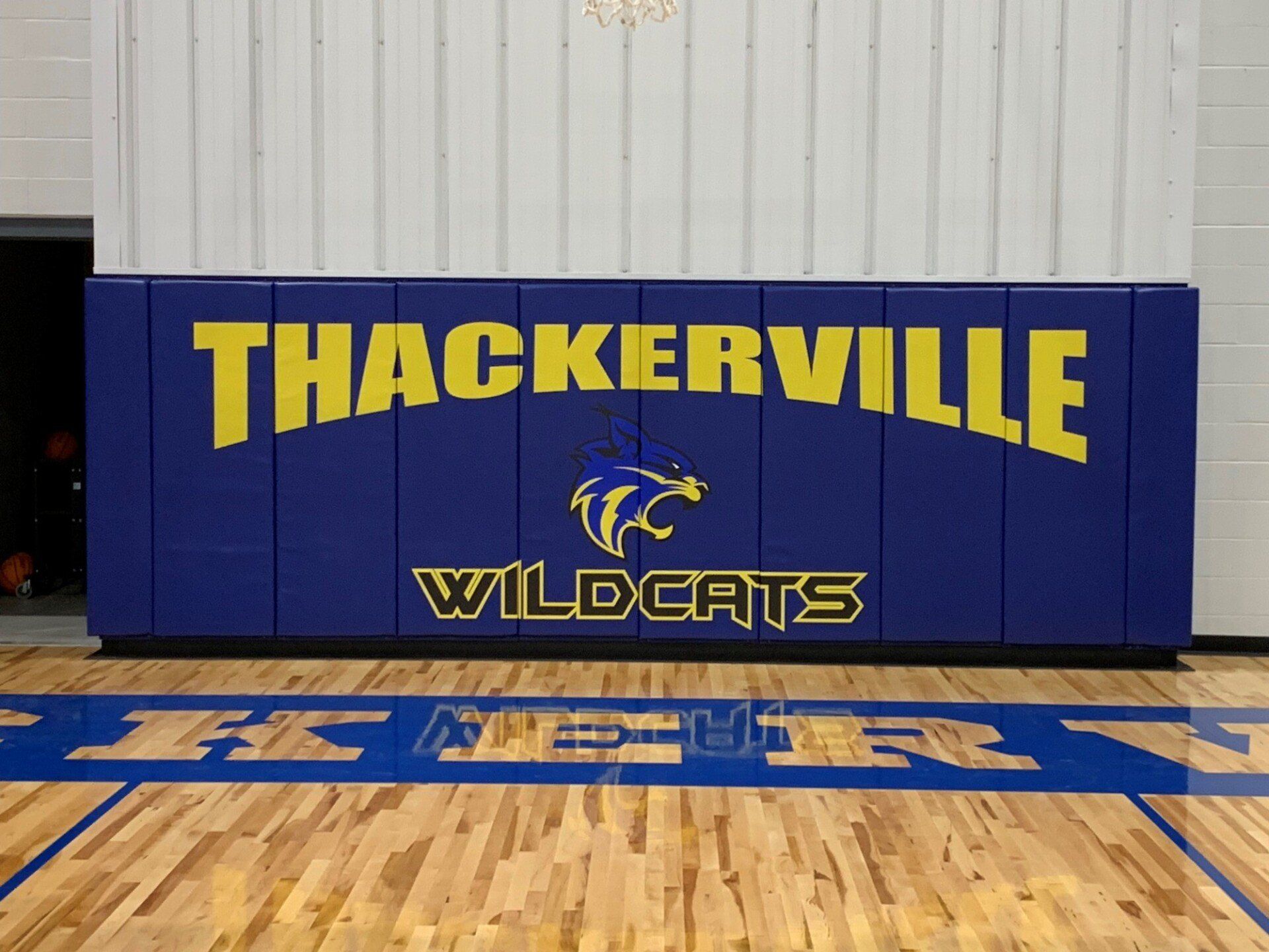 Thackerville Wildcats banner on a gym wall above a basketball court, in blue and yellow.