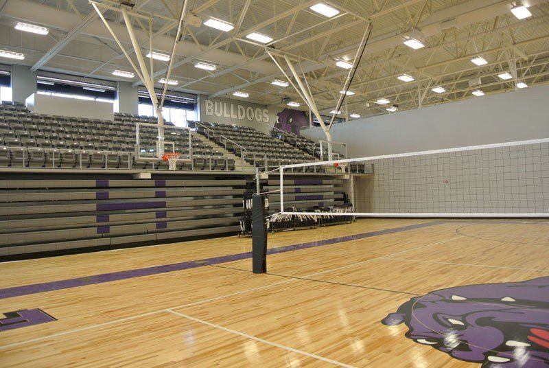 Indoor gym with volleyball net, bleachers, and hardwood floor with bulldog logo