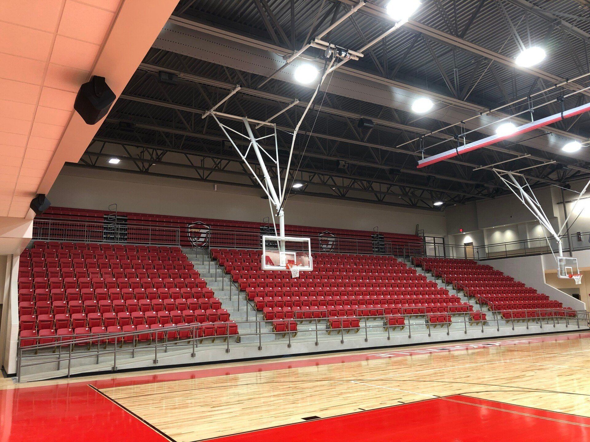 Indoor basketball court with red bleachers and a centered hoop under bright ceiling lights