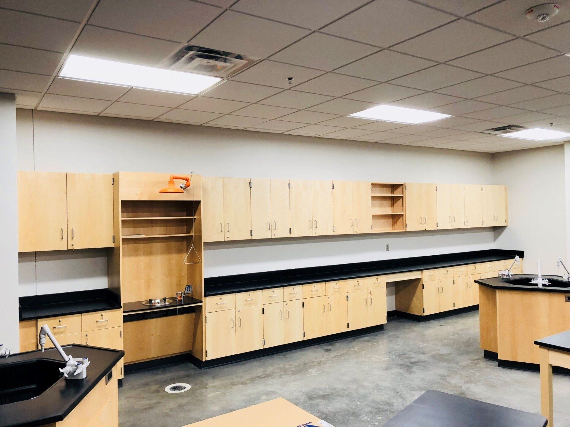 Empty science classroom with beige cabinets, black countertops, and lab sinks under fluorescent ceiling lights