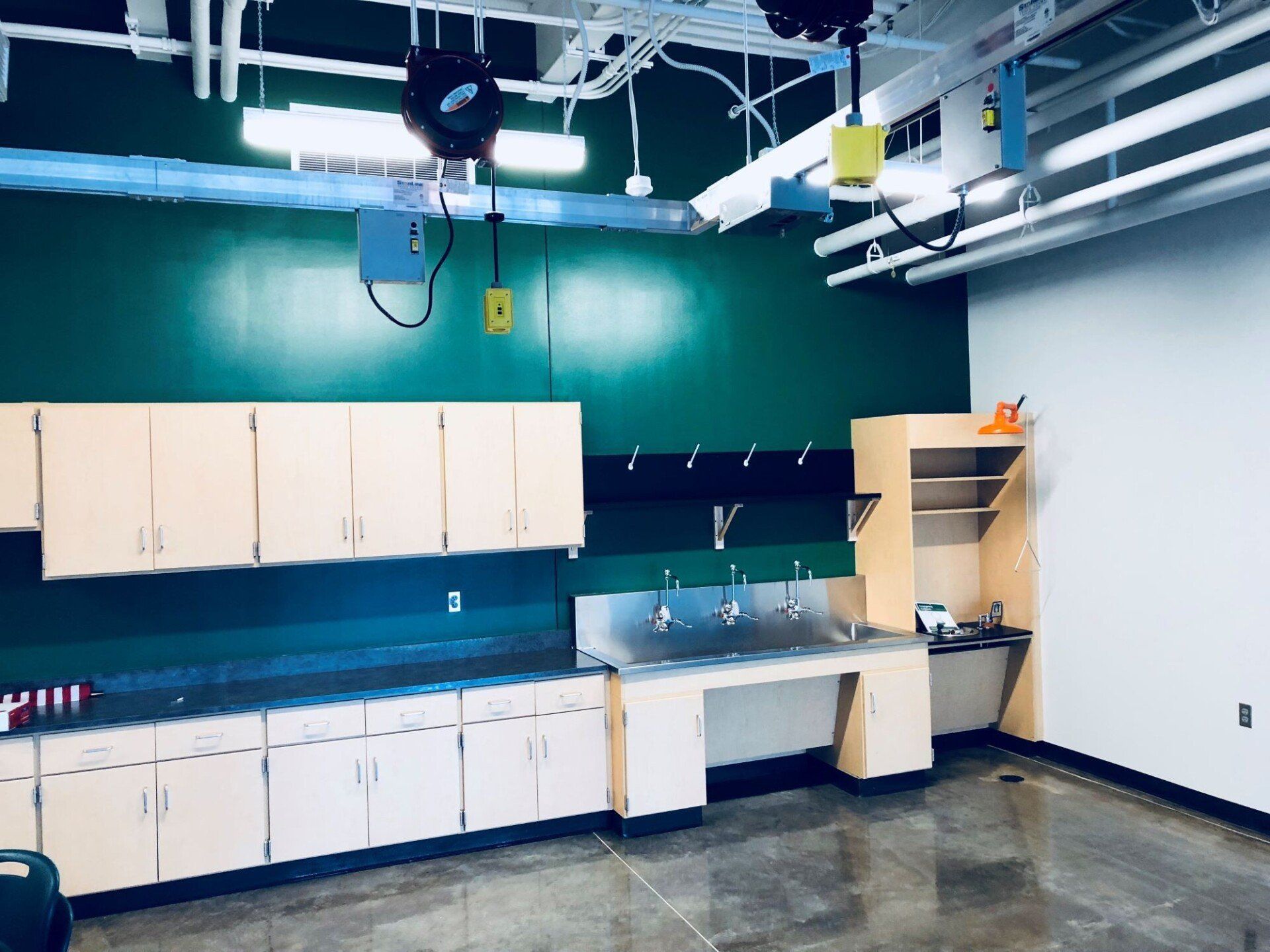 Empty classroom lab with teal walls, white cabinets, sinks, and exposed ceiling pipes
