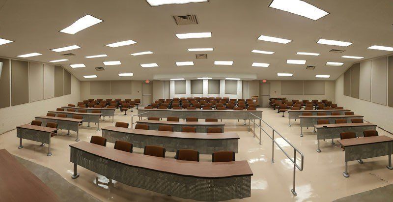 Empty modern lecture hall with curved rows of desks, beige walls, and bright ceiling lights