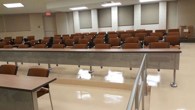Empty classroom with rows of brown chairs and desks under fluorescent ceiling lights
