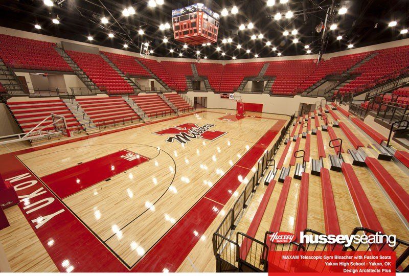 Empty basketball arena with red seating and polished wood court, viewed from the stands