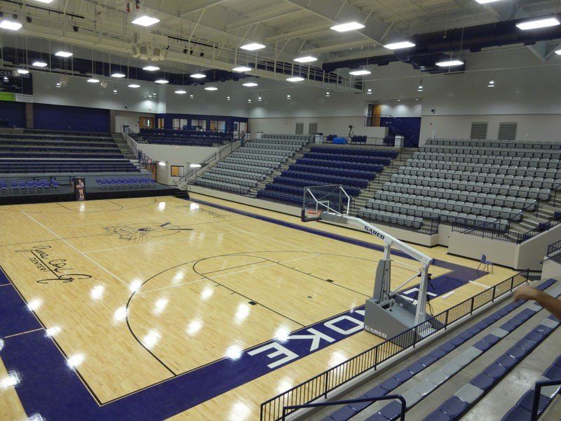 Empty indoor basketball arena with blue seating, polished wood court, and overhead lights