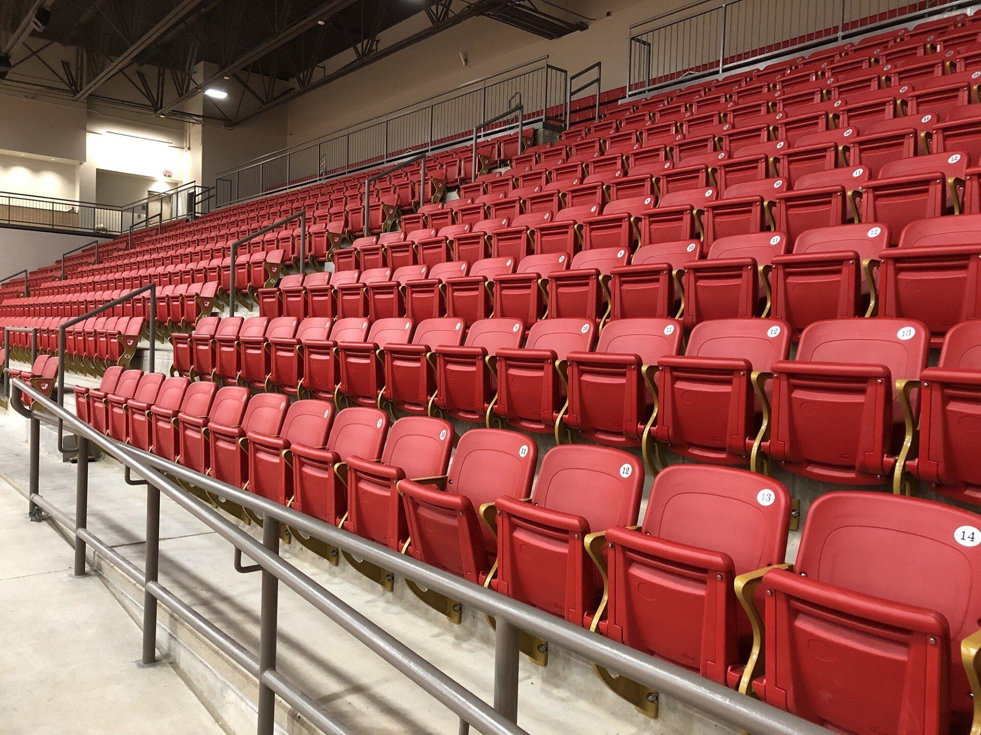 Rows of empty red stadium seats in an indoor arena, viewed from the side.