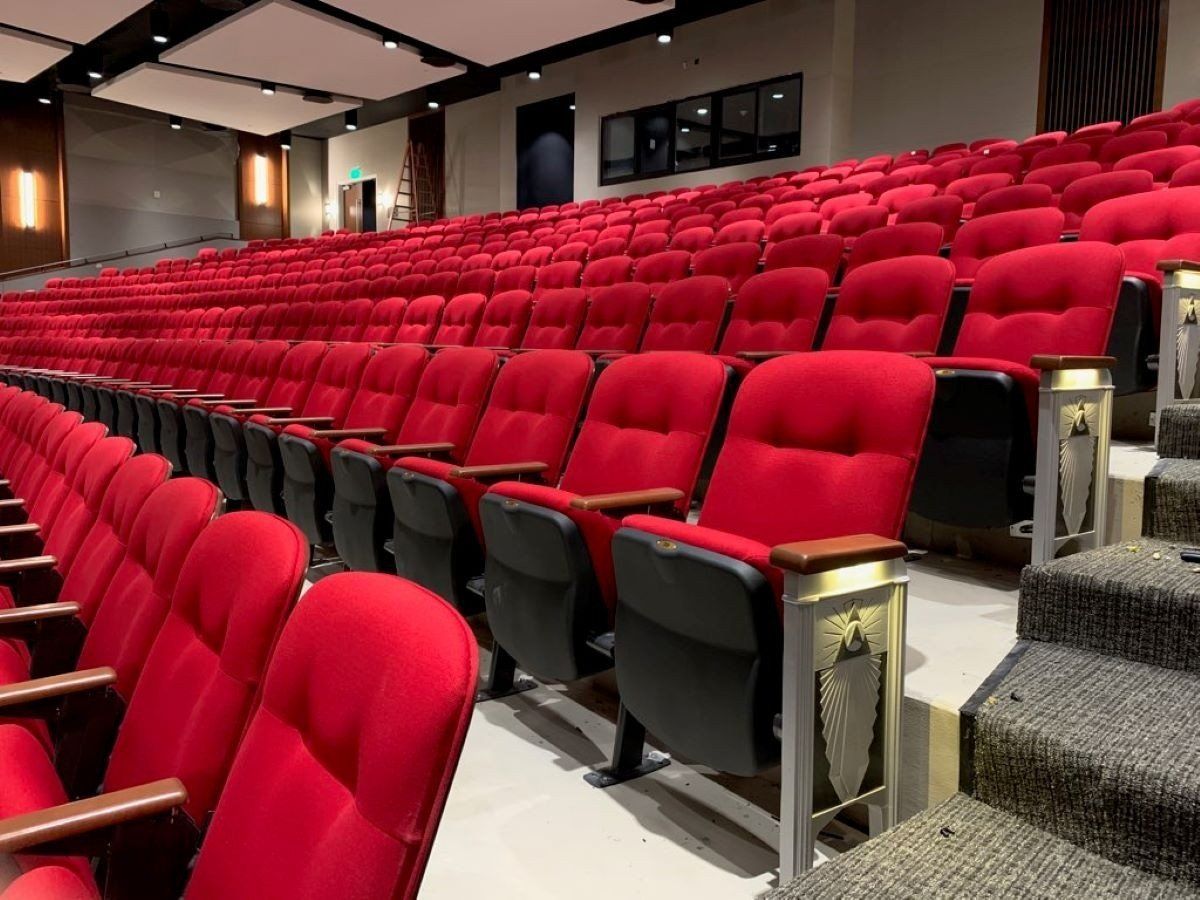 Empty theater auditorium with rows of red seats and stairs along the aisle