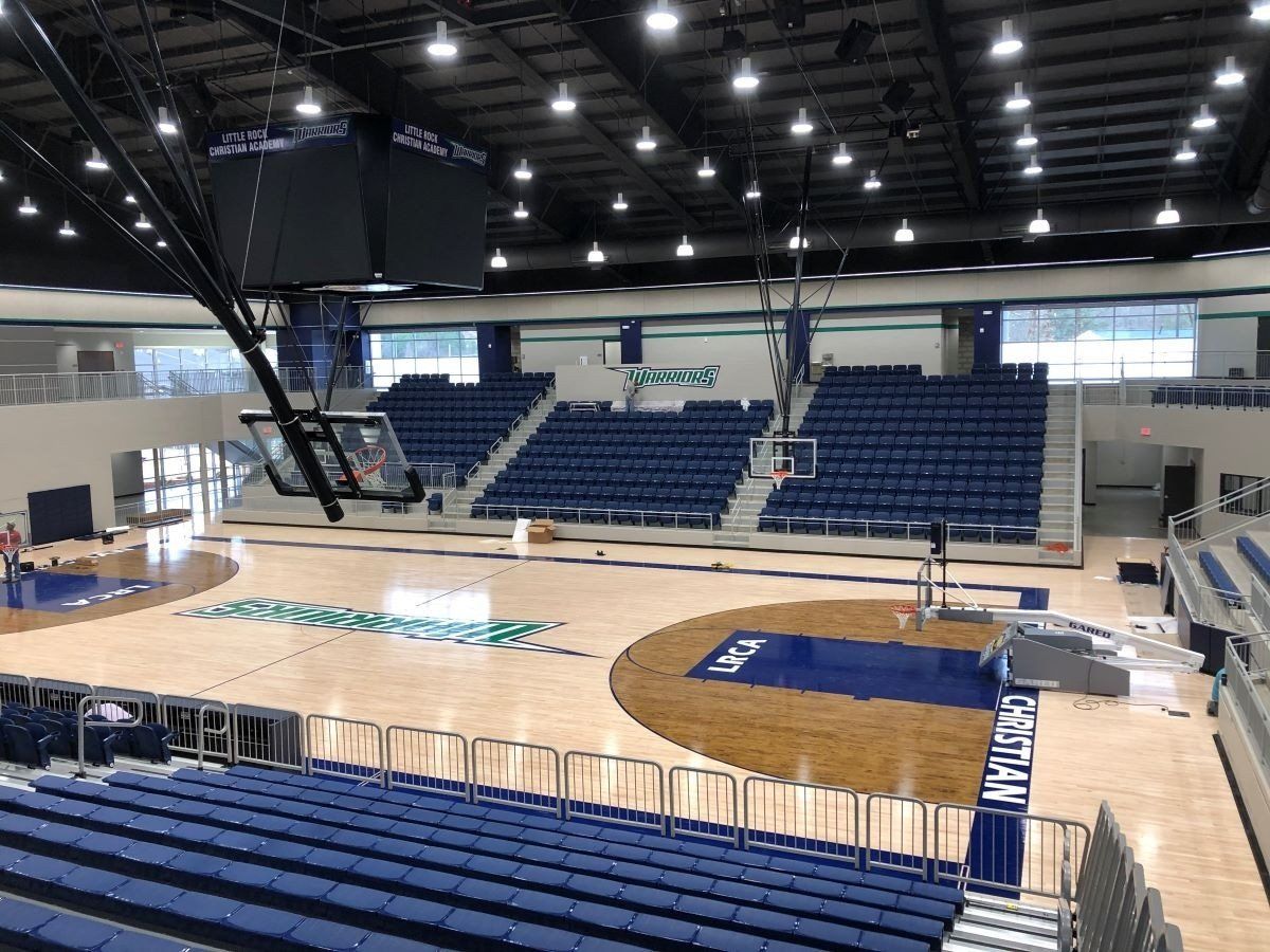 Empty indoor basketball arena with blue bleachers and polished wood court under bright ceiling lights