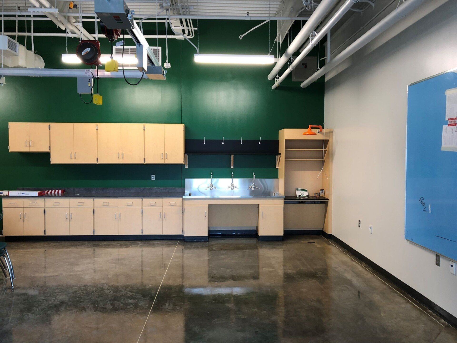 Empty workshop with beige cabinets, green wall, polished floor, and blue bulletin board