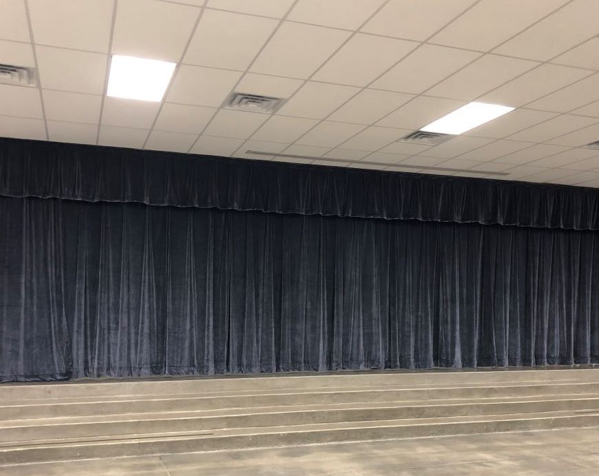 Empty room with a long dark stage curtain, drop ceiling, and patterned carpeted floor