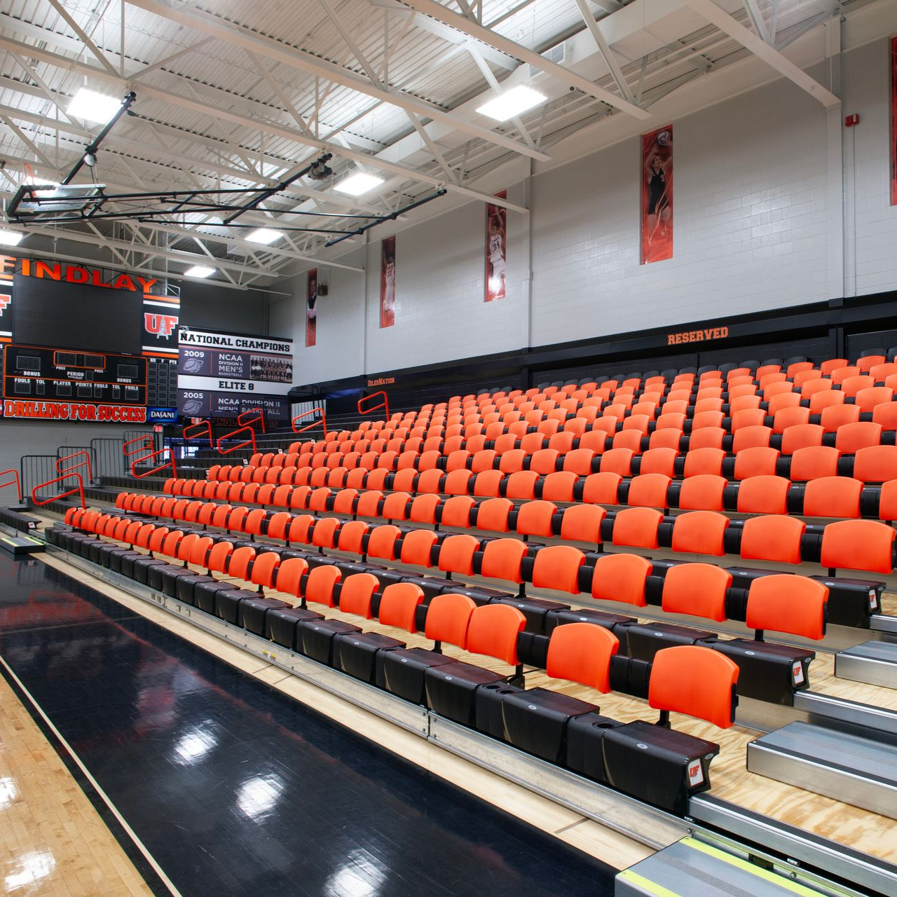 Indoor basketball arena with rows of orange seats and a polished black court sideline