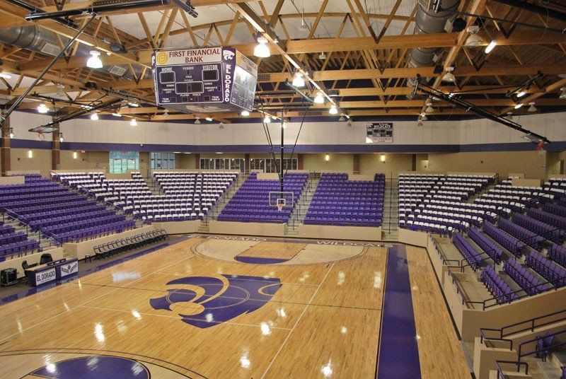 Empty indoor basketball arena with purple seating and a polished court viewed from center court