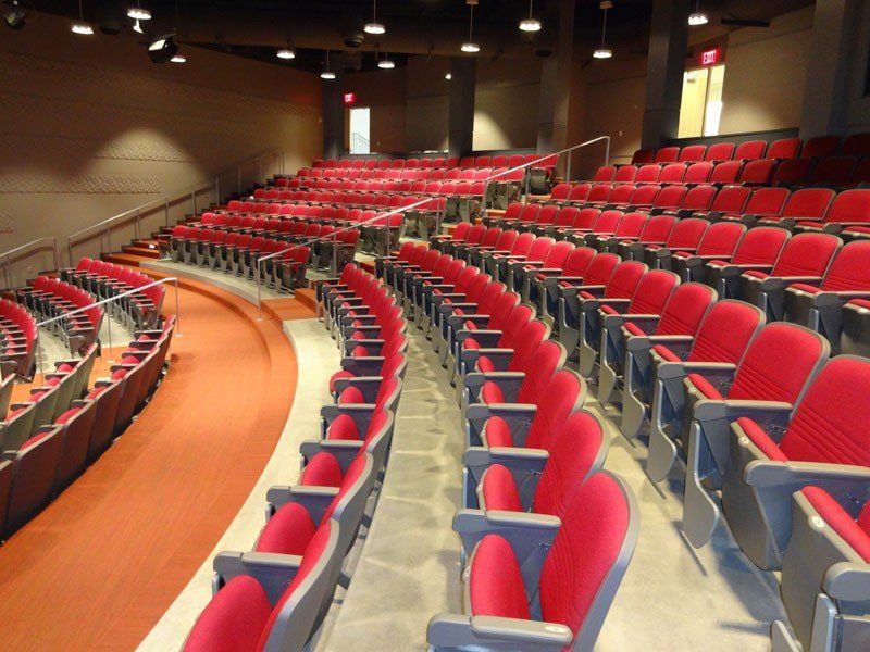 Empty U of A auditorium with rows of red seats and curved aisles under warm lighting