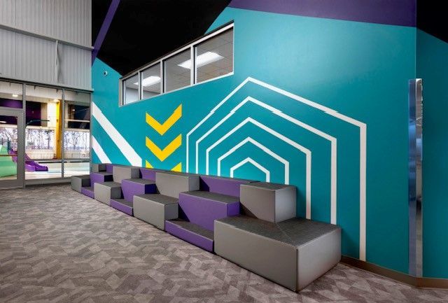 Modern lounge with purple-gray seating, teal wall, and geometric white and yellow wall art