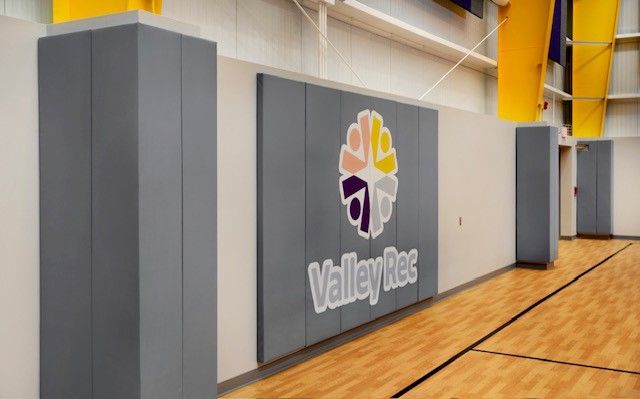 Valley High gym wall with school logo beside a basketball court and padded columns