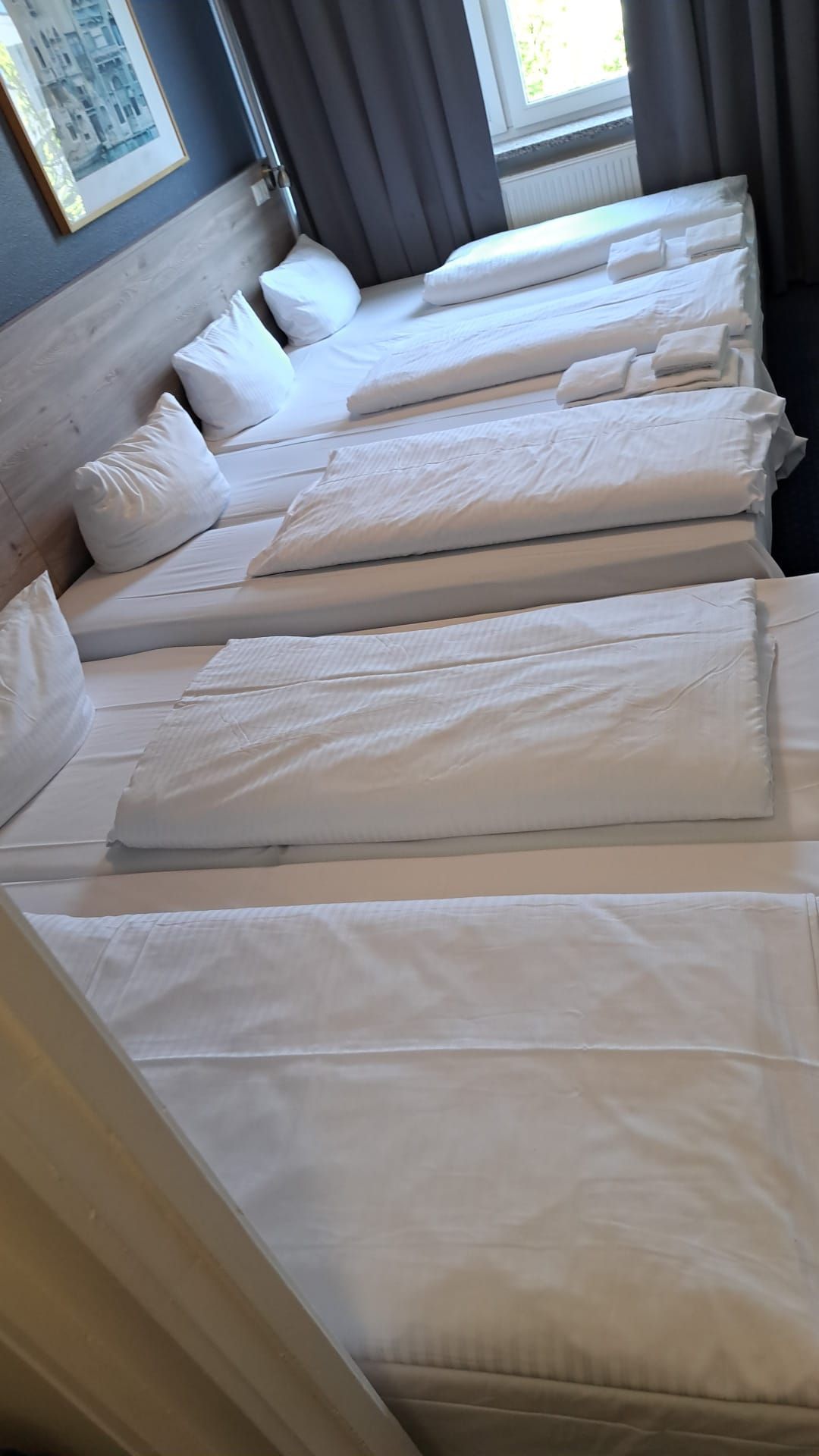 Eine Reihe von Betten in einem Hotelzimmer mit weißen Laken und Kissen.