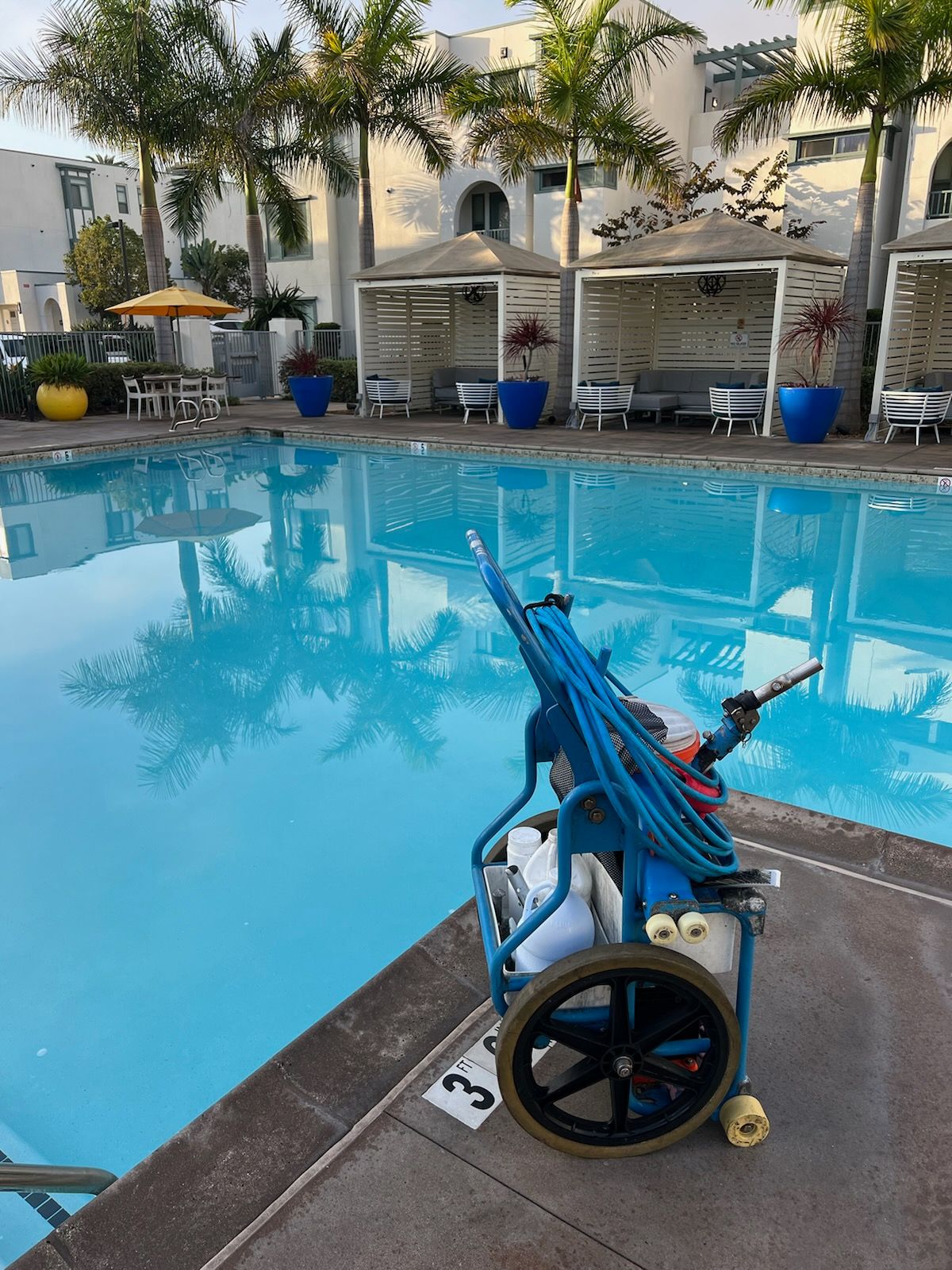 A cart with a hose attached to it is sitting next to a swimming pool.