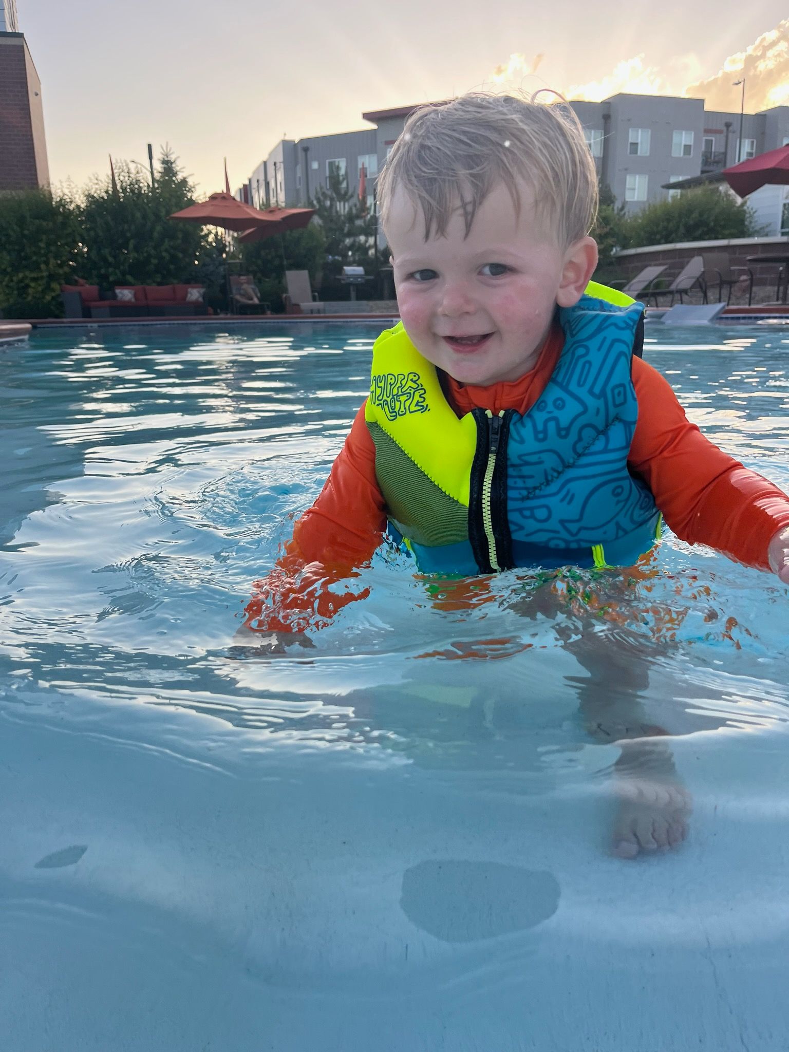A little boy wearing a life jacket is swimming in a pool.