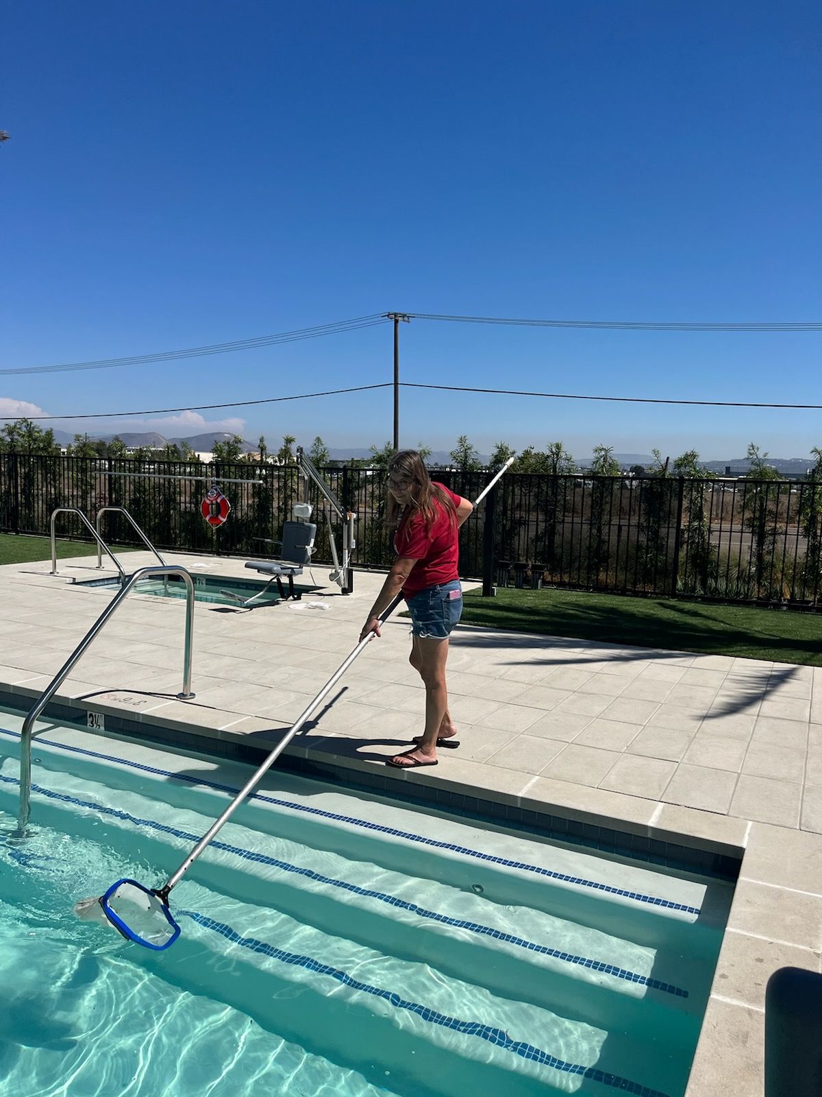 A woman is cleaning a swimming pool with a broom.