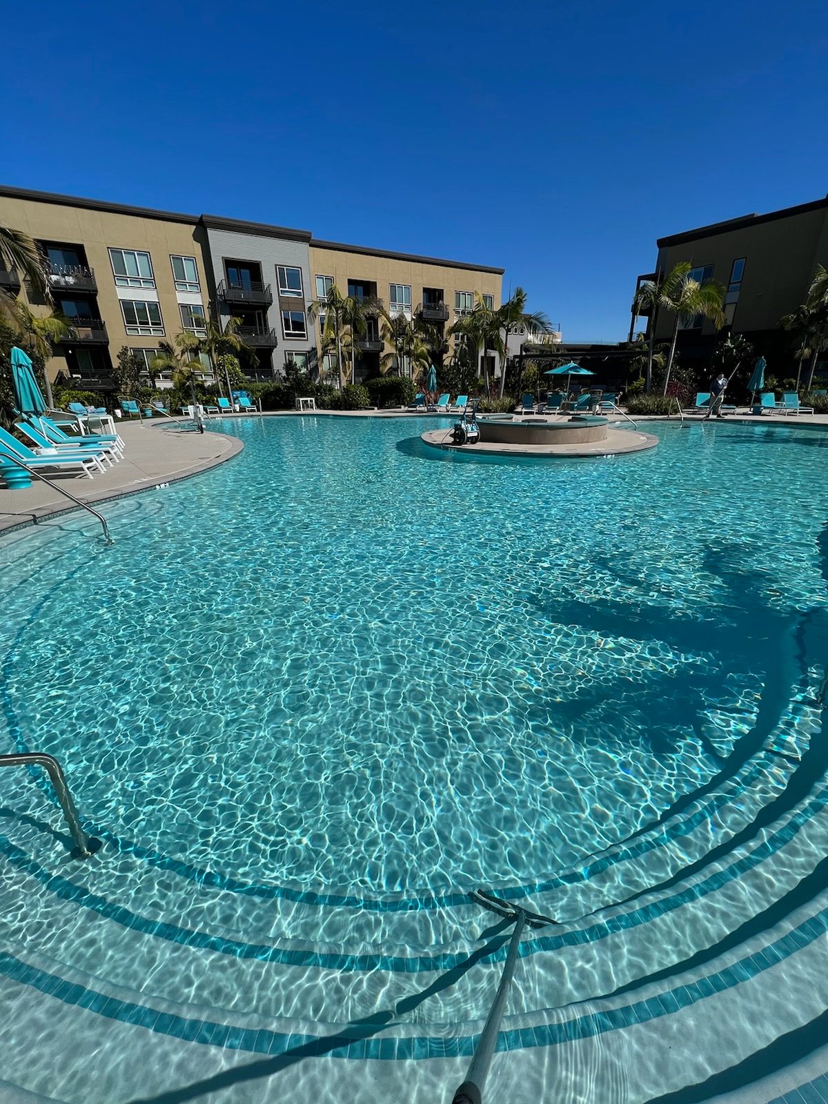 A large swimming pool surrounded by chairs and umbrellas in front of a building.