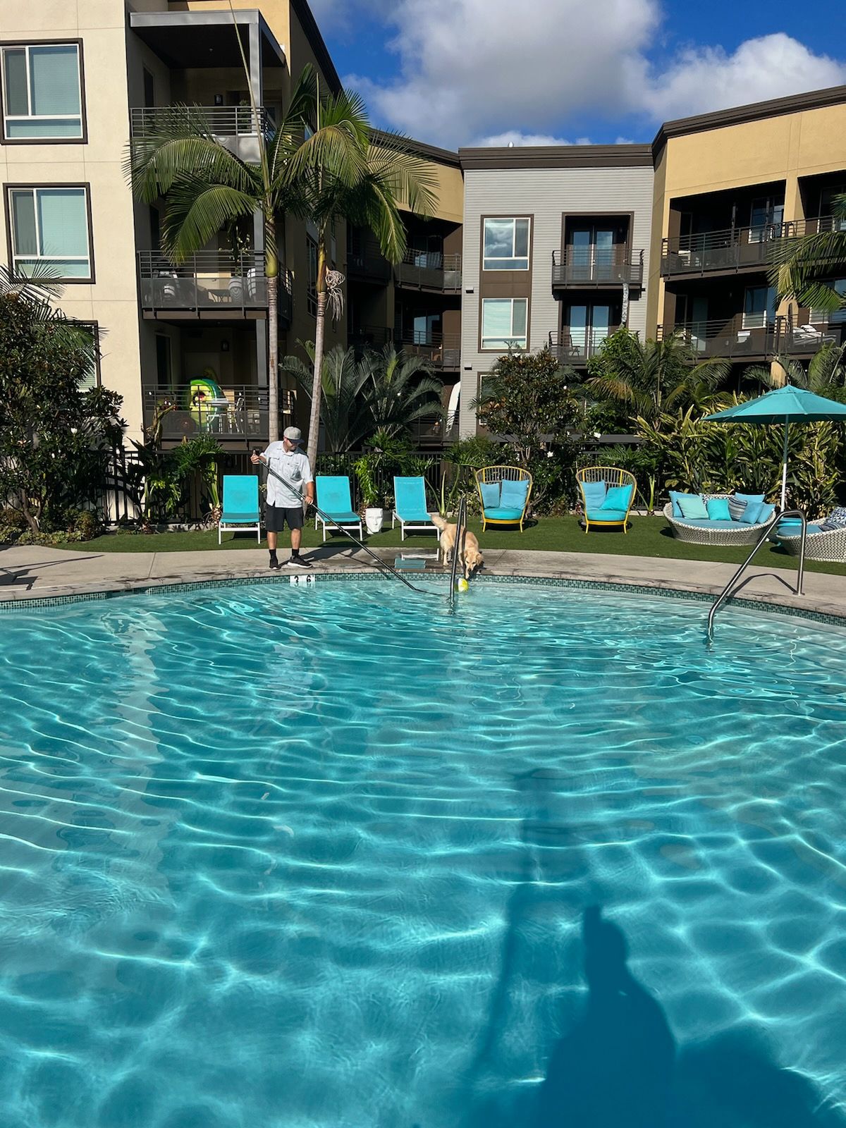 A man is standing next to a swimming pool in front of a building.