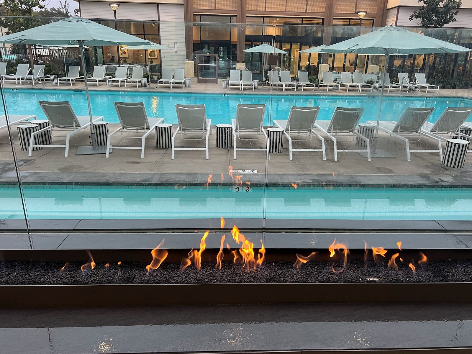 A swimming pool with chairs and umbrellas and a fire pit in front of it.