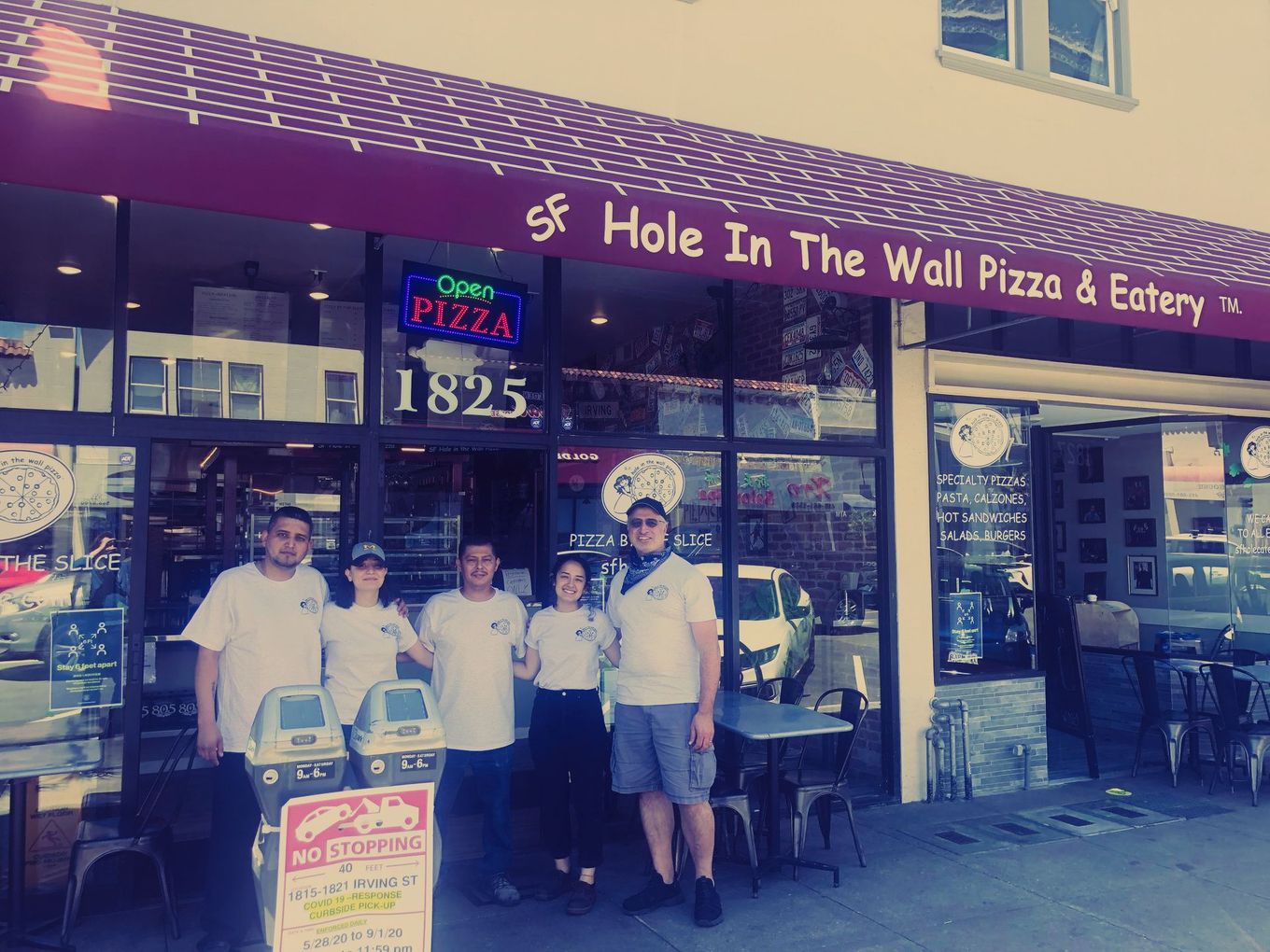 A group of people standing in front of a hole in the wall pizza and eatery