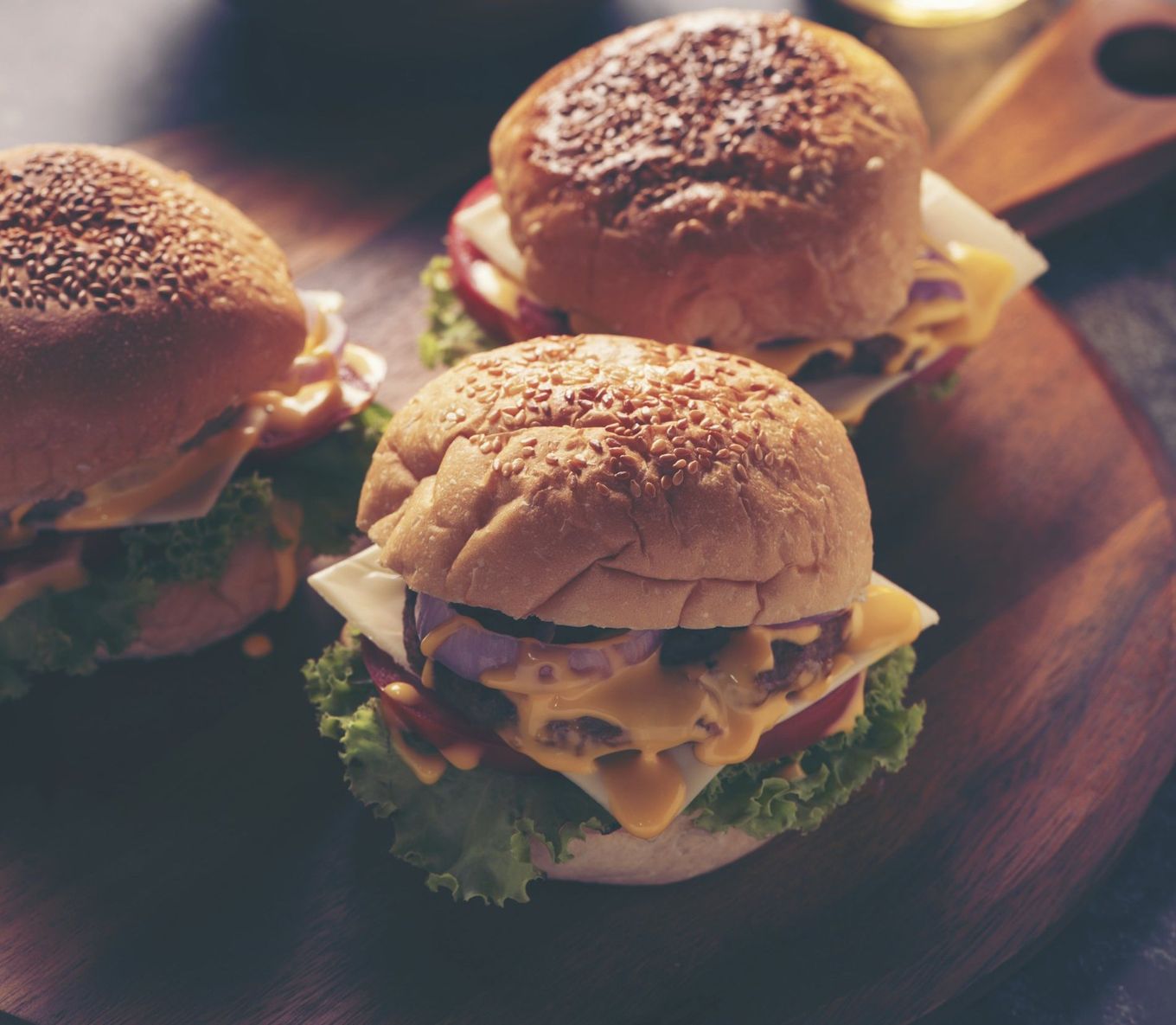 Three hamburgers are sitting on a wooden cutting board